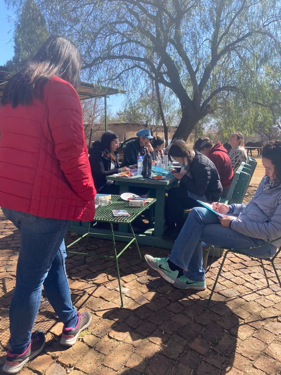 Workshop participants writing at outdoor tables under a tree